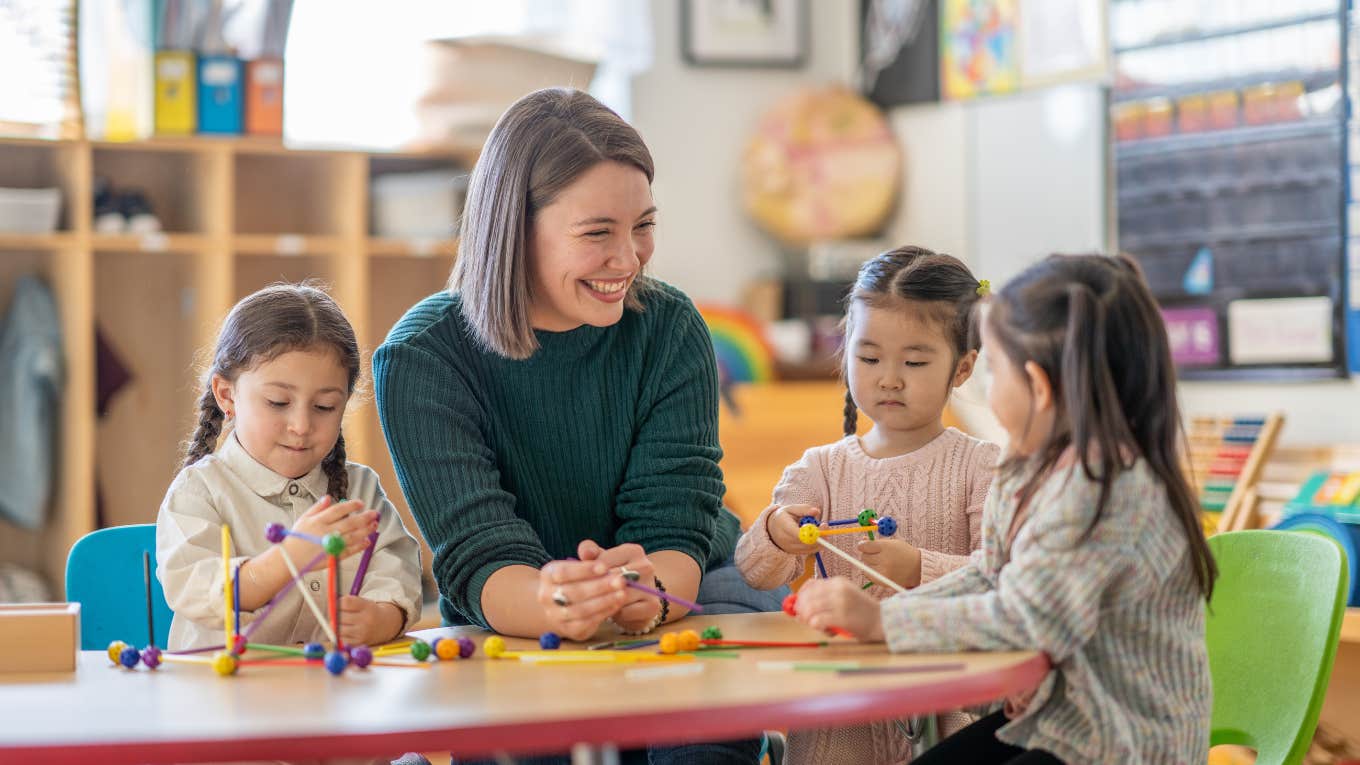 Teacher Claims Teaching Is No Longer About Education But Rather Is A Customer Service Job teacher smiling at students playing with educational toys at their desks